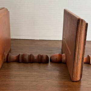 May include: A pair of wooden bookends with a simple design. Each bookend has a rectangular base and a curved top. The bookends are made of dark brown wood and have a natural finish.