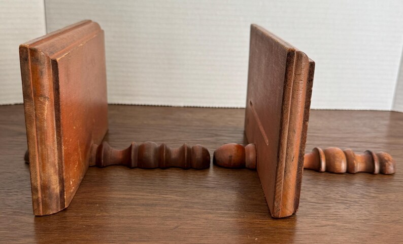 May include: A pair of wooden bookends with a simple design. Each bookend has a rectangular base and a curved top. The bookends are made of dark brown wood and have a natural finish.