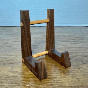Könnte beinhalten: Ein Holzständer mit zwei horizontalen Holzstiften. Der Ständer ist dunkelbraun mit einer natürlichen Holzoptik.
