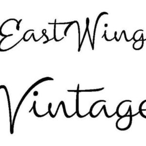 May include: Black and white cursive script text that reads "East Wing Vintage".