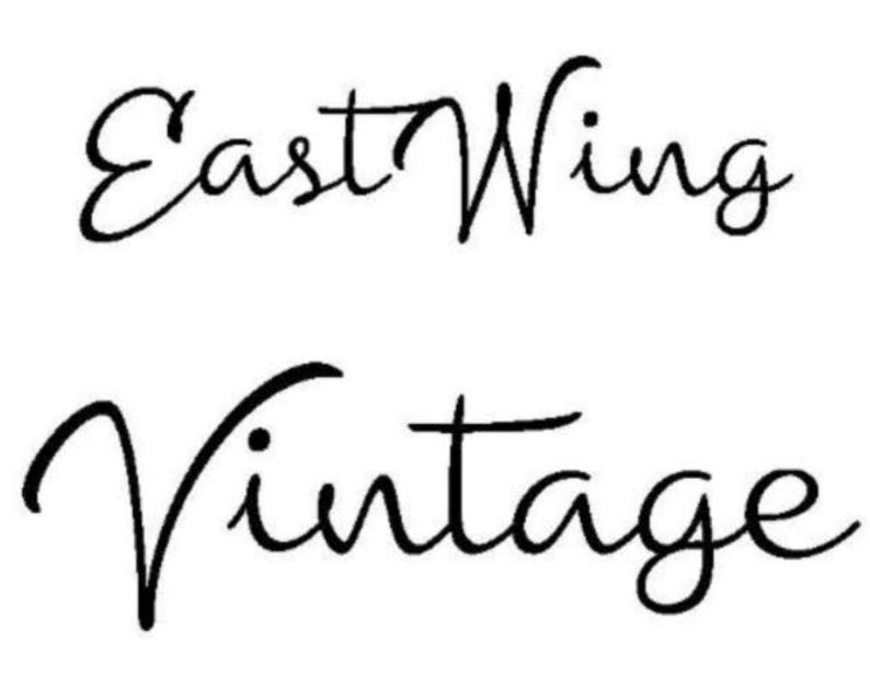 May include: Black and white cursive script text that reads "East Wing Vintage".