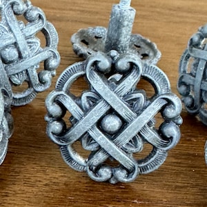 May include: Set of six silver metal cabinet knobs with a decorative, intricate design. Each knob features a circular base with a woven pattern and a raised center.