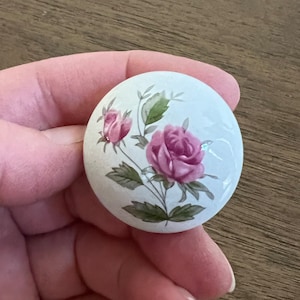May include: White ceramic knob with a pink rose and green leaves design.