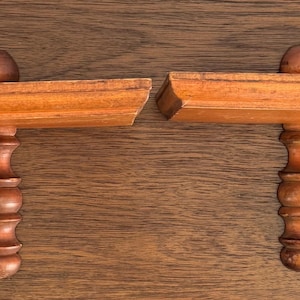 May include: Two wooden shelf brackets with a decorative, turned, spindle design. The brackets are made of light brown wood and have a simple, traditional style.