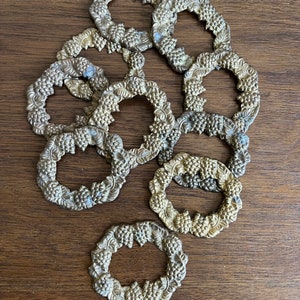 K&ouml;nnte beinhalten: Ein Set aus zehn goldfarbenen Serviettenringen mit einem Traubenmuster. Die Ringe sind verziert und detailliert, mit einer runden Form und einem erhabenen Design.