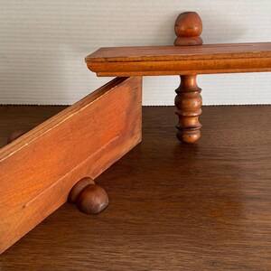 May include: Two wooden shelves with decorative turned wooden legs. The shelves are made of unfinished wood and have a natural wood grain.