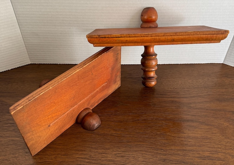 May include: Two wooden shelves with decorative turned wooden legs. The shelves are made of unfinished wood and have a natural wood grain.