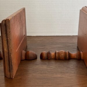 May include: Two wooden bookends with a simple design. Each bookend has a decorative, turned wooden base.