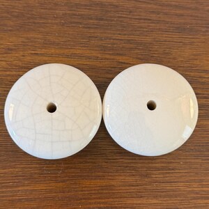 May include: Two white ceramic knobs with a crackled glaze finish and a small hole in the center.