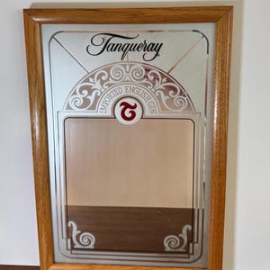 May include: A rectangular mirror with a wooden frame. The mirror features the Tanqueray logo and the words "IMPORTED ENGLISH GIN". The design includes decorative scrollwork and a red "G" symbol.