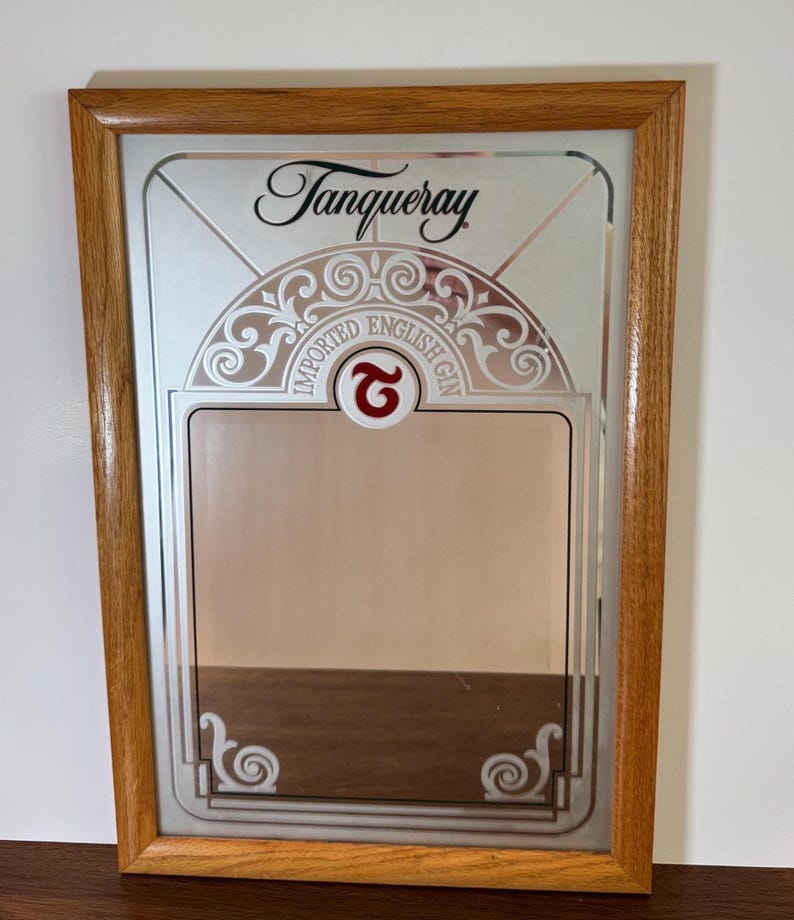 May include: A rectangular mirror with a wooden frame. The mirror features the Tanqueray logo and the words "IMPORTED ENGLISH GIN". The design includes decorative scrollwork and a red "G" symbol.