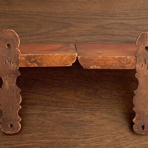 May include: A pair of wooden shelves with decorative, carved brackets. The shelves are made of natural wood with a warm brown colour.