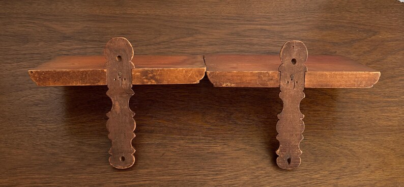 May include: A pair of wooden shelves with decorative, carved brackets. The shelves are made of natural wood with a warm brown colour.