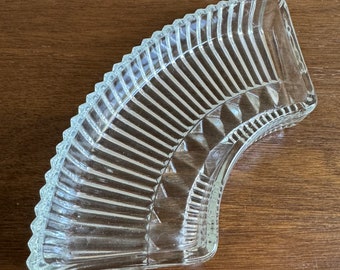 Puede incluir: Un plato de vidrio transparente con un diseño en forma de abanico. El plato tiene una superficie texturizada y un borde curvo.