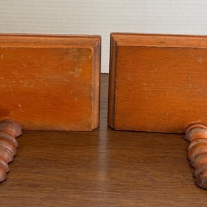 May include: A pair of wooden bookends with a twisted design. The bookends are a light brown colour and have a rectangular shape.