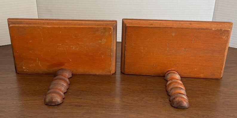 May include: A pair of wooden bookends with a twisted design. The bookends are a light brown colour and have a rectangular shape.