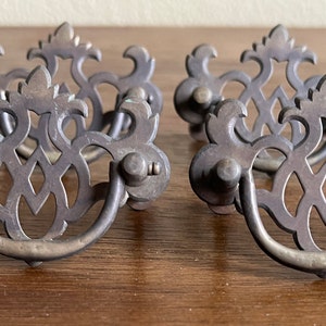 May include: Set of five antique brass drawer pulls with intricate, ornate designs. Each pull features a decorative, openwork design with a curved handle.