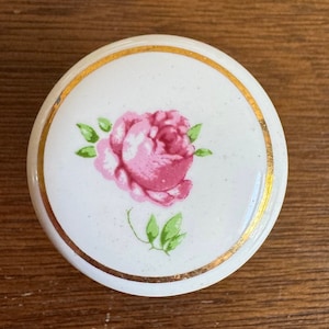 May include: A white ceramic knob with a gold rim and a pink rose design.