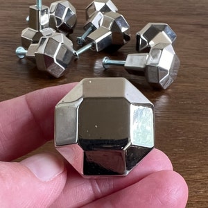 May include: Set of six silver-toned cabinet knobs with a geometric, faceted design. Each knob has a single screw hole for installation.