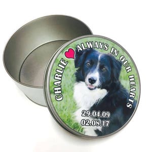 May include: A silver metal tin with a lid. The lid displays a photo of a black and white dog, the text "CHARLIE" and "ALWAYS IN OUR HEARTS", a pink heart, and the dates 29.04.09 and 02.08.17. The tin is open.
