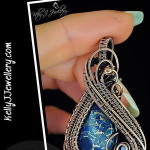 Könnte beinhalten: Handgefertigtes Anhänger-Tutorial mit dem Titel "Celeste" von Kelly J Jewellery. Der Anhänger zeigt einen tropfenförmigen blauen Stein mit einem einzigartigen Muster, der in aufwendiger Kupferdrahtweberei eingefasst ist. Das Design umfasst dekorative Wirbel und einen kleinen blauen Akzentstein.