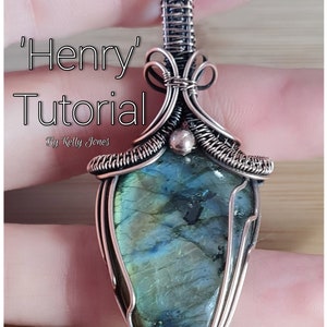 May include: A silver wire wrapped pendant featuring a green and blue labradorite gemstone. The pendant is shaped like a teardrop and has a bail at the top. The pendant is labelled 'Henry' Tutorial by Kelly Jones'.