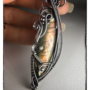 K&ouml;nnte beinhalten: Ein silberner, drahtgewickelter Anh&auml;nger mit einem schillernden Labradorit-Edelstein. Der Anh&auml;nger hat die Form einer Tr&auml;ne und ein zartes, filigranes Design. Der Anh&auml;nger wurde von Kelly J Jewellery hergestellt.