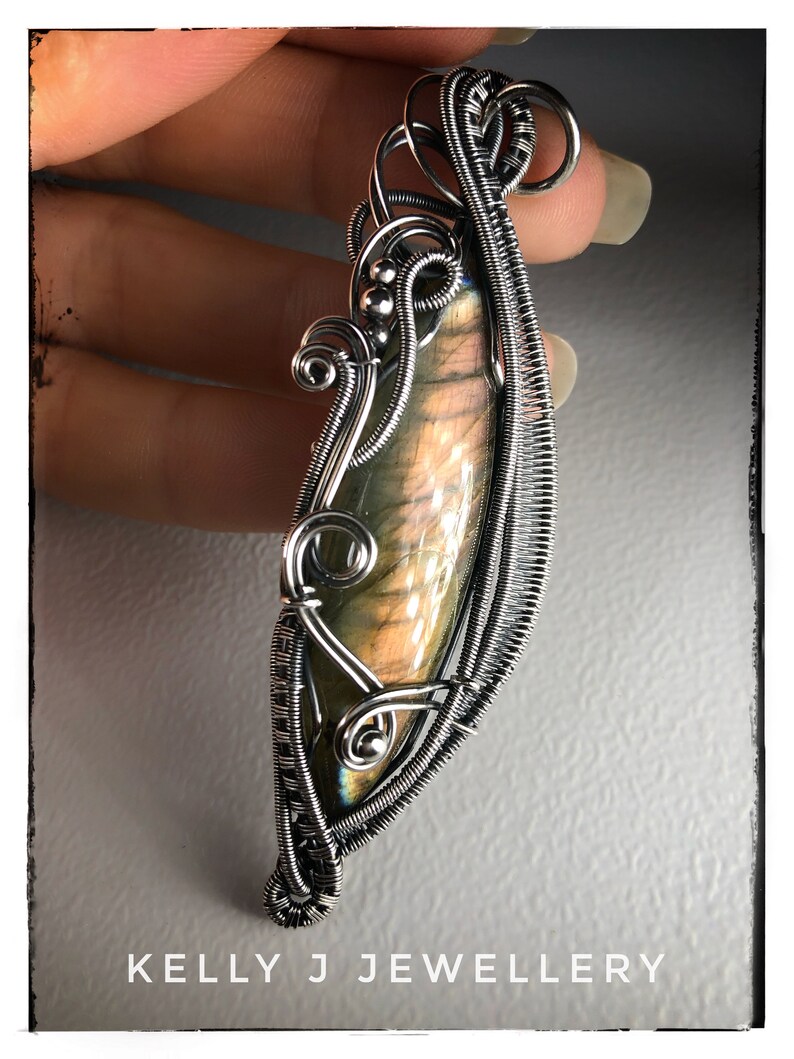 K&ouml;nnte beinhalten: Ein silberner, drahtgewickelter Anh&auml;nger mit einem schillernden Labradorit-Edelstein. Der Anh&auml;nger hat die Form einer Tr&auml;ne und ein zartes, filigranes Design. Der Anh&auml;nger wurde von Kelly J Jewellery hergestellt.