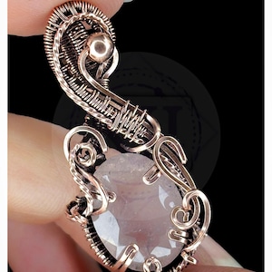 May include: A wire-wrapped pendant featuring a faceted, oval-shaped pale pink gemstone encased in intricate copper wire coils and swirls. The design includes a prominent copper bead at the top and the text KELLY J JEWELLERY at the bottom.
