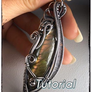 May include: A silver wire wrapped pendant featuring a green and iridescent gemstone. The pendant is held in a hand and the word "Tutorial" is visible in the bottom right corner of the image.