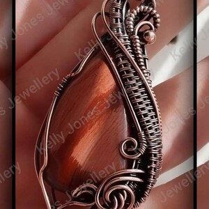 May include: A copper wire wrapped pendant featuring a red tiger's eye stone. The pendant is made with intricate wire weaving and has a unique, organic design.