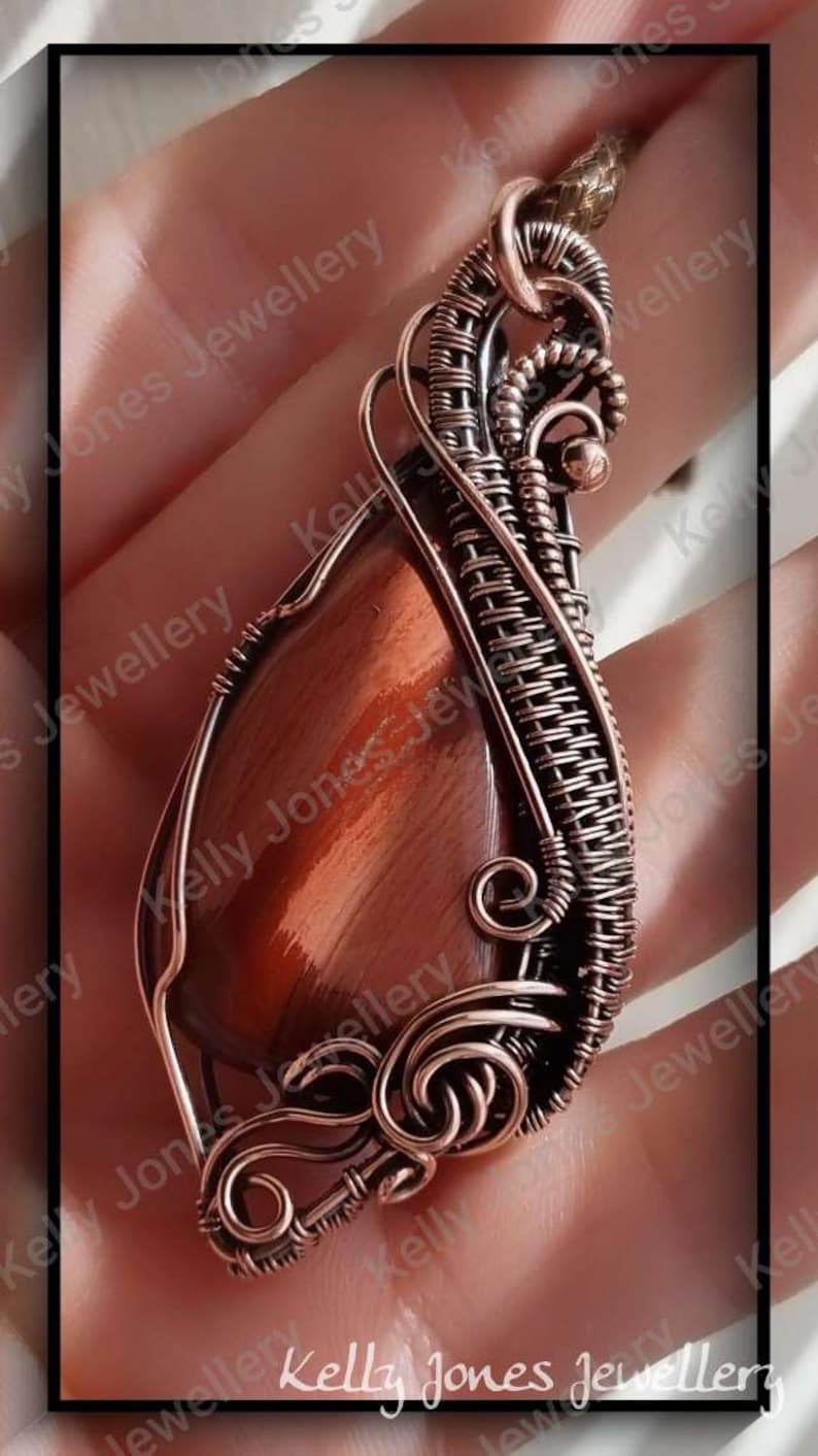 May include: A copper wire wrapped pendant featuring a red tiger's eye stone. The pendant is made with intricate wire weaving and has a unique, organic design.