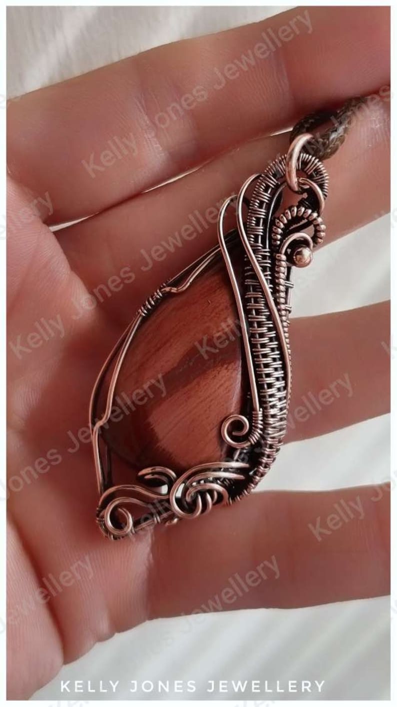 May include: A copper wire wrapped pendant featuring a red tiger's eye stone. The pendant is handmade and has a unique, intricate design.