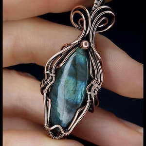 Könnte beinhalten: Handgefertigter Anhänger mit einem tropfenförmigen Labradorit-Edelstein, umwickelt mit Kupferdraht. Der Draht bildet kunstvolle Wirbel und Muster um den Stein. Der Text "KELLY J JEWELLERY" ist unten zu sehen.