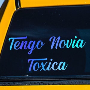 May include: A yellow truck with a blue and purple sticker on the back window that says "Tengo Novia Toxica".