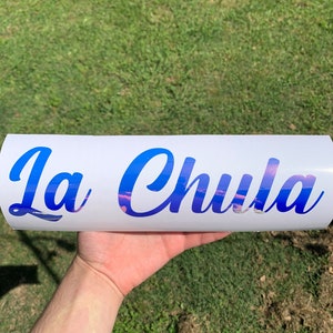 Pu&ograve; includere: Un adesivo in vinile bianco con il testo "La Chula" in lettere corsive blu. Le lettere hanno un effetto sfumato con uno schema di colori rosa e blu.