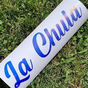 Pu&ograve; includere: Un adesivo in vinile bianco con il testo "La Chula" in lettere blu iridescenti.