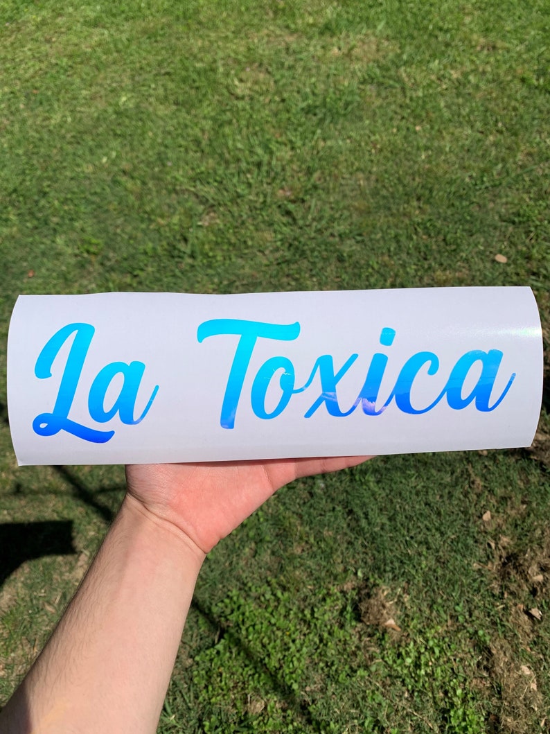 Pu&ograve; includere: Un adesivo in vinile bianco con il testo "La Toxica" in un font con sfumatura blu.