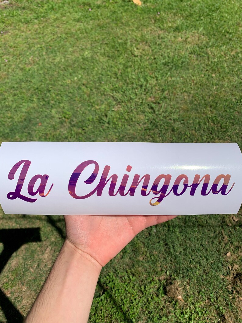 Pu&ograve; includere: Adesivo in vinile bianco con il testo "La Chingona" in un font sfumato viola e rosa.