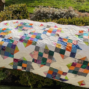 May include: A patchwork quilt featuring a white background with a repeating star pattern composed of multi-coloured fabric squares. The quilt displays a variety of vibrant colours including orange, blue, green, and purple, with intricate swirl quilting.