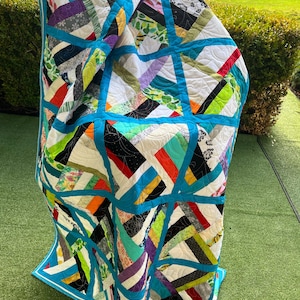 May include: A vibrant quilt with a geometric pattern. It showcases a patchwork of diverse fabrics in shades of white, blue, green, orange, and purple. The quilt is edged with a bright turquoise border.