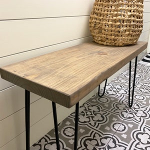 May include: A rustic wooden console table with a natural finish. The tabletop is supported by black hairpin legs. A woven basket sits on the table. The table is approximately 48 inches long.
