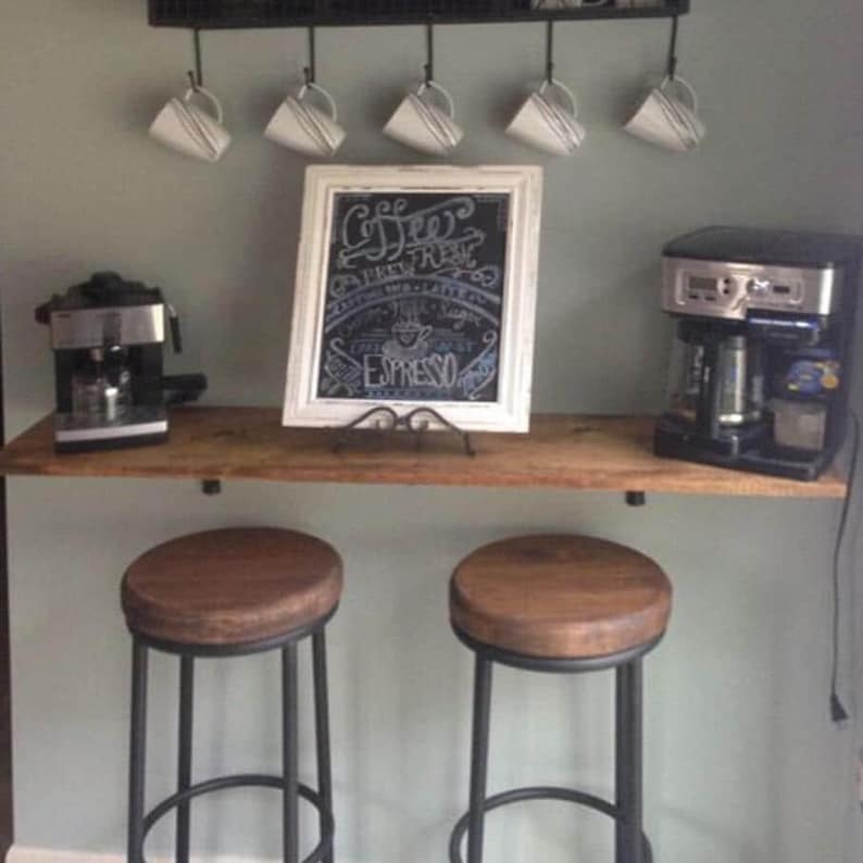 Puede incluir: Una estaci&oacute;n de caf&eacute; con una estanter&iacute;a de madera, dos taburetes y una pizarra con la inscripci&oacute;n "Coffee, Fresh, Espresso". Hay dos cafeteras, seis tazas colgantes y un estante de metal negro.