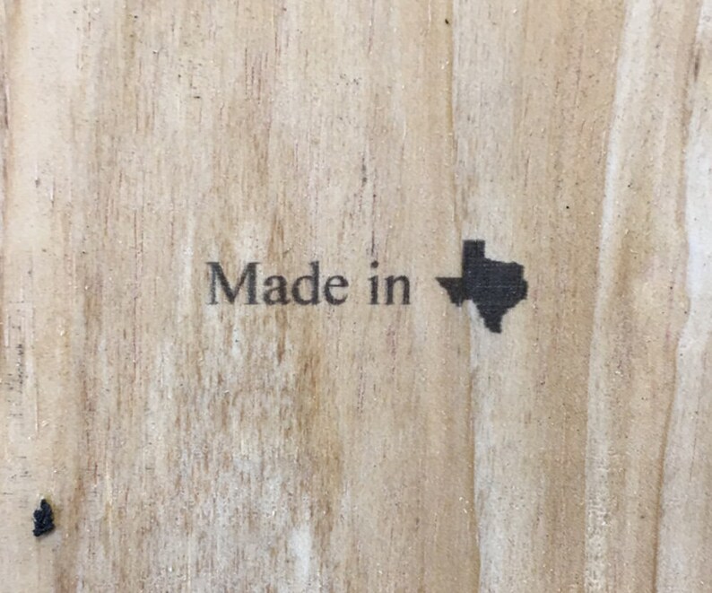 May include: Close-up of a wooden surface with the words "Made in" and a silhouette of the state of Texas printed in black. The wood grain is visible.
