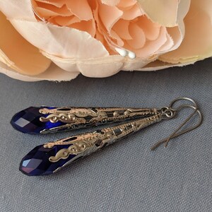 Vintage Style earrings with long silver tone filigree bead caps over sapphire blue faceted glass beads.