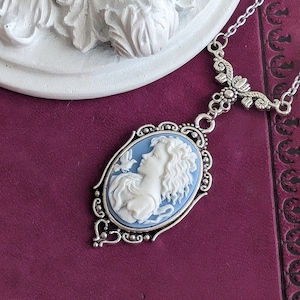 A close up of a blue and white cameo necklace with an ornate silver pendant and tulip connector displayed on a vintage book.