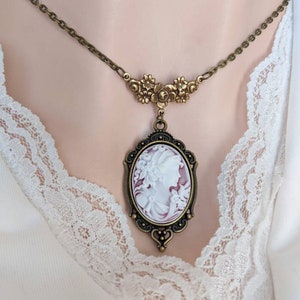 A neckline image of a cameo necklace in antiqued bronze finish. Cameo features a Grecian Goddess with a small bird set in a finely detailed setting suspended by a floral connector. The cameo colour is white on a wine background.