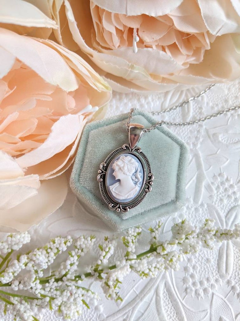 Cameo necklace. Silver Oval setting with flourishes on a stainless steel chain. The cameo is of a Greek Goddess with a light blue background and detailed white relief.