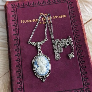 A close up of a blue and white cameo necklace with an ornate silver pendant and tulip connector displayed on a vintage book.