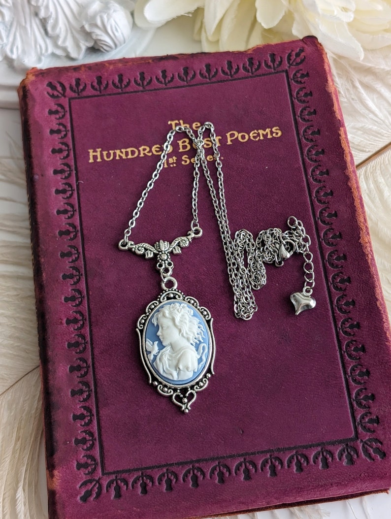 A close up of a blue and white cameo necklace with an ornate silver pendant and tulip connector displayed on a vintage book.